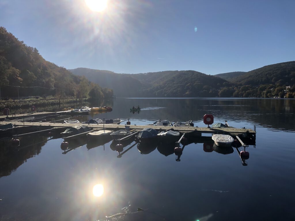 Ein Anlegesteg für kleine Boote, im Hintergrund kleine Berge bei Sonnenschein.